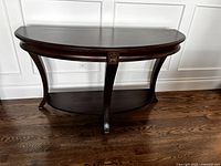 Front view of demilune console table showing half-moon top, apron carving and curved legs.