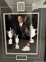 Framed display showing Tiger Woods in a suit with four silver trophy replicas, the PGA Tour logo above, and engraved plaque below with 'Tiger Woods Tiger Slam'.