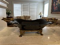 Side view showing the black porcelain bowl with golden brass claw feet and a handle on one side