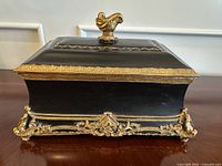 Side view showing ornate gold decorative accents and feet, black body, and minor scuff.