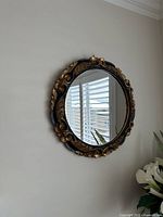 Front view of round ornate black and gold framed mirror hanging on wall.