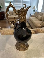 Porcelain wine decanter with black round body and ornate golden handle and base captured from front angle
