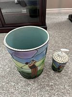Photo showing the waste basket and soap dispenser side by side on carpeted floor, highlighting the stained glass style golfer artwork.