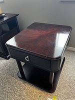 Angle view of wooden night table showing rounded corners, drawer with metal ring pull, and bottom shelf.
