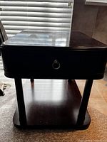 Front view of dark wood night table showing drawer with metal ring handle and bottom shelf.