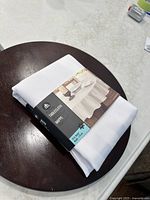 Folded white round tablecloth with label, new in packaging.