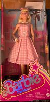 Front view of Barbie doll in original packaging showing pink gingham dress, facial features, and packaging design.