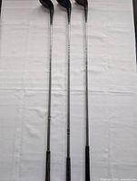 Three golf driver clubs laid side by side showing full length with metal shafts and black grips