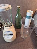 Full view of the blender, green glass bottle, ceramic vase, and clear glass vase together on fabric surface