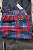 Top photo showing folded pants: navy joggers, red and blue plaid sleep pants and gray pants underneath, with tags visible