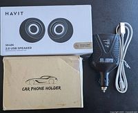 Photo showing boxed Havit SK486 2.0 USB speakers, a beige car phone holder box, black Motor Master power converter adapter, and a white USB-C charging cable.