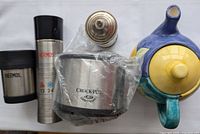 All items in the lot shown together: Little Crock Pot dipper wrapped in plastic, two Thermos containers, vintage metal container, and Barbados handmade teapot.