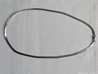 Full length of the silver herringbone chain necklace on a white textured fabric.