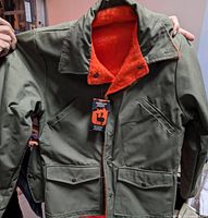 Front view of the 1985 unisex reversible bomber winter jacket showing olive green exterior, front pockets, snap buttons, and orange fleece lining inside.