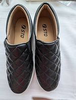 Top-down view of the pair of new women's black slip-on shoes with quilted pattern and padded interior insoles showing brand STQ.