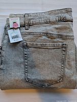 Folded pair of light grey wash women's denim jeans with visible back pocket and attached tags.