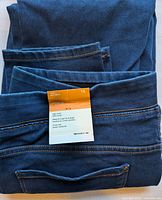 Folded view of the dark blue denim jeans with an attached size and care tag indicating size 16 and features such as high waist and gentle rise.