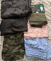 Lot of five women's bottoms: two camouflage pants, black skirt, pink shorts with hearts, blue floral pajama pants, and two pairs of patterned tights in packaging.