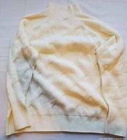 Cream colored knitted women's sweater laid flat, showing front detail and collar.