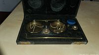 Full view of the antique balance scale and weights set in the open black case showing scale pans, beam, and weights.