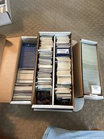 Three large boxes filled with baseball cards, sorted and stacked vertically in rows. Cards include different brands and years noted on labels.