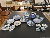 Wide angle showing entire assortment of blue and white ceramic and porcelain dishware on black table