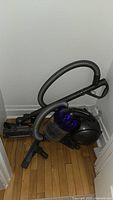 Full view of Dyson DC37 canister vacuum with hose and main floor head attached, showing purple cyclone dust container and black spherical canister body.