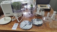 Wide shot showing entire food processor base with attachments and multiple slicing/shredding discs spread out on table.