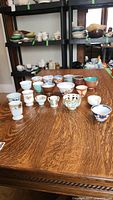 Multiple miniature bowls and cups arranged on table, two rows show 18 small porcelain and ceramic pieces