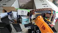Photo of the contents in baskets and boxes showing an assortment of office and electronic items including keyboard, camera box, cables, and pens.