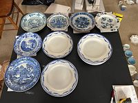 Table display of 8 matching blue-bordered plates alongside 6 assorted decorative plates