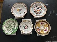 Top-down view of all five plates displaying diverse floral and leaf patterns and sizes.