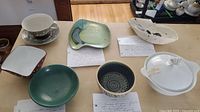 Overview of vintage pottery and porcelain items on table including bowls, pitcher, lidded container, and dish.