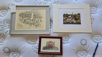 Wide view showing three prints arranged on a surface: two larger prints, one framed and matted, the other matted only, and a smaller framed print.