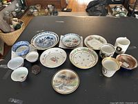 Overview of all items on black table, including cups, saucers, bowls and glass piece