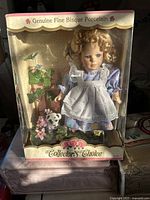 Front view of the boxed bisque porcelain doll with floral background and dog figurine.