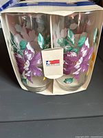 Front view of two floral glass tumblers in original box showing purple flowers and green leaves design, USA made sticker visible