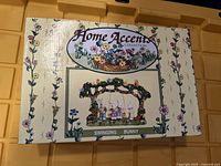 Box front showing Home Accents branding and image of ceramic swinging bunny figurine with floral decoration and bunnies on a swing.