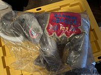 Gray plush elephant in original plastic packaging, side view showing blanket with embroidered text.