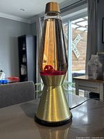 Front angled view of the lava lamp showing amber liquid and red wax inside the conical glass container with gold-colored base and top.