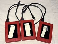 Photo shows three red external hard drives with black front panels, each labeled with their storage capacities: two labeled 1TB and one labeled 500GB. Each drive has an attached USB 3.0 cable.
