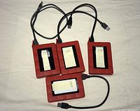 Four red external hard drives with USB 3.0 cables attached, three labeled 1 TB and one labeled 500 GB, arranged on a white cloth background.
