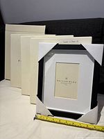 Five Pottery Barn black wood gallery photo frames, four still in original white protective packaging boxes, one frame unpackaged showing front. Measuring tape shown for approximate size reference.