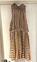 Front view of sleeveless pink and brown polka dot dress hanging on hanger, showing high neckline and gathered skirt.