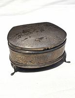 Closed antique silver snuff box with visible tarnishing and legs shown from front side angle.