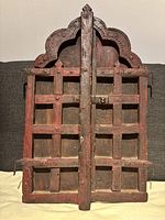 Front view of antique wooden window shutters showing carved top and steel grid reinforcements.