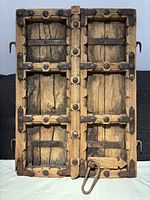 Front view of antique Indian wooden shutters showing wood planks, steel straps, rivets, and hooks