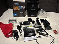 Full lot contents including GoPro Hero 3 camera, original boxes, accessories, batteries, charging cables, mounts, memory card and manual spread out on gray background.