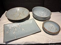 Set of one rectangular serving plate and three ceramic bowls with cherry blossom patterns on white cloth.