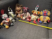 Six different original Lion King Broadway stuffed animals arranged on grey couch, showing full front details and size comparison using a yellow measuring tape.